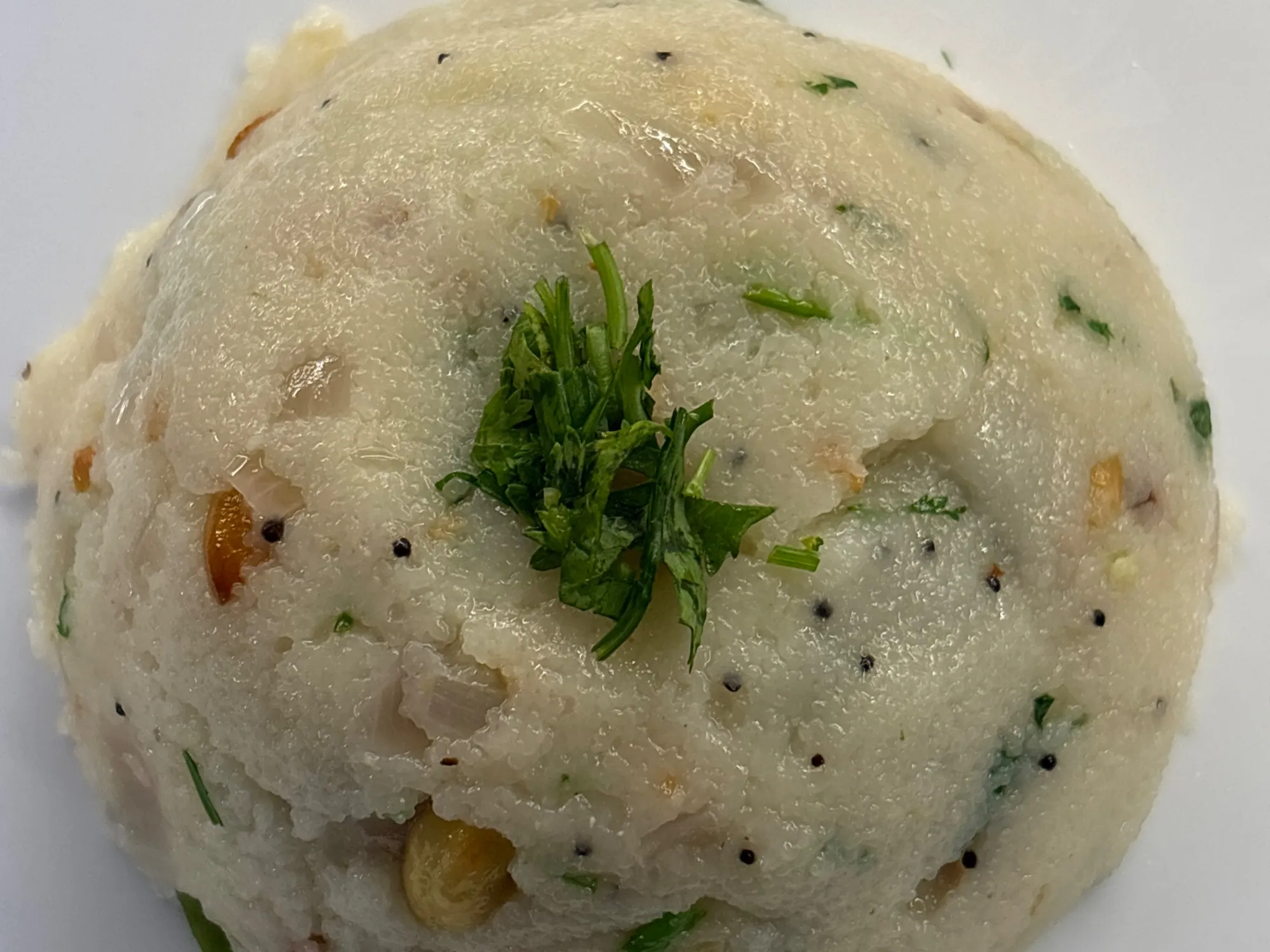 A bowl of pale golden ghee upma topped with fried cashews and chopped coriander, a lemon wedge at the side