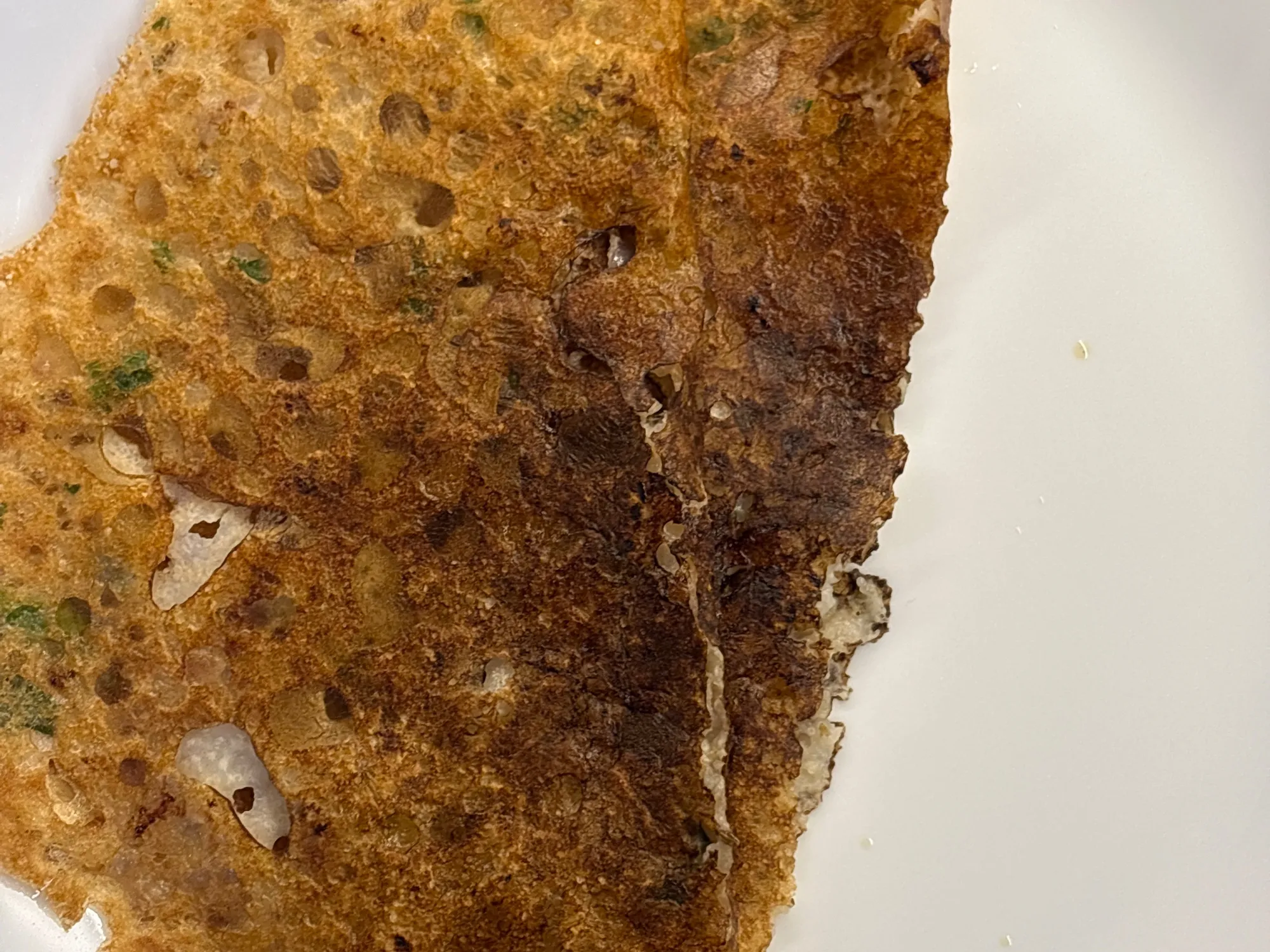 A lacy golden dosa with holes across it, folded on a steel plate beside chutney