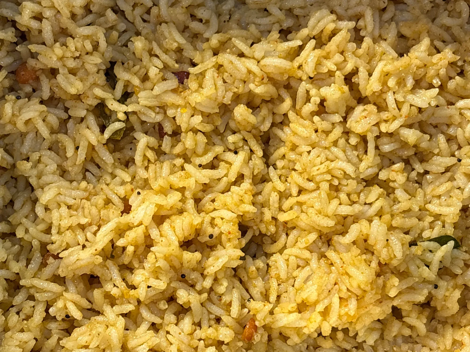 A plate of pale yellow tamarind rice studded with peanuts, chana dal and curry leaves