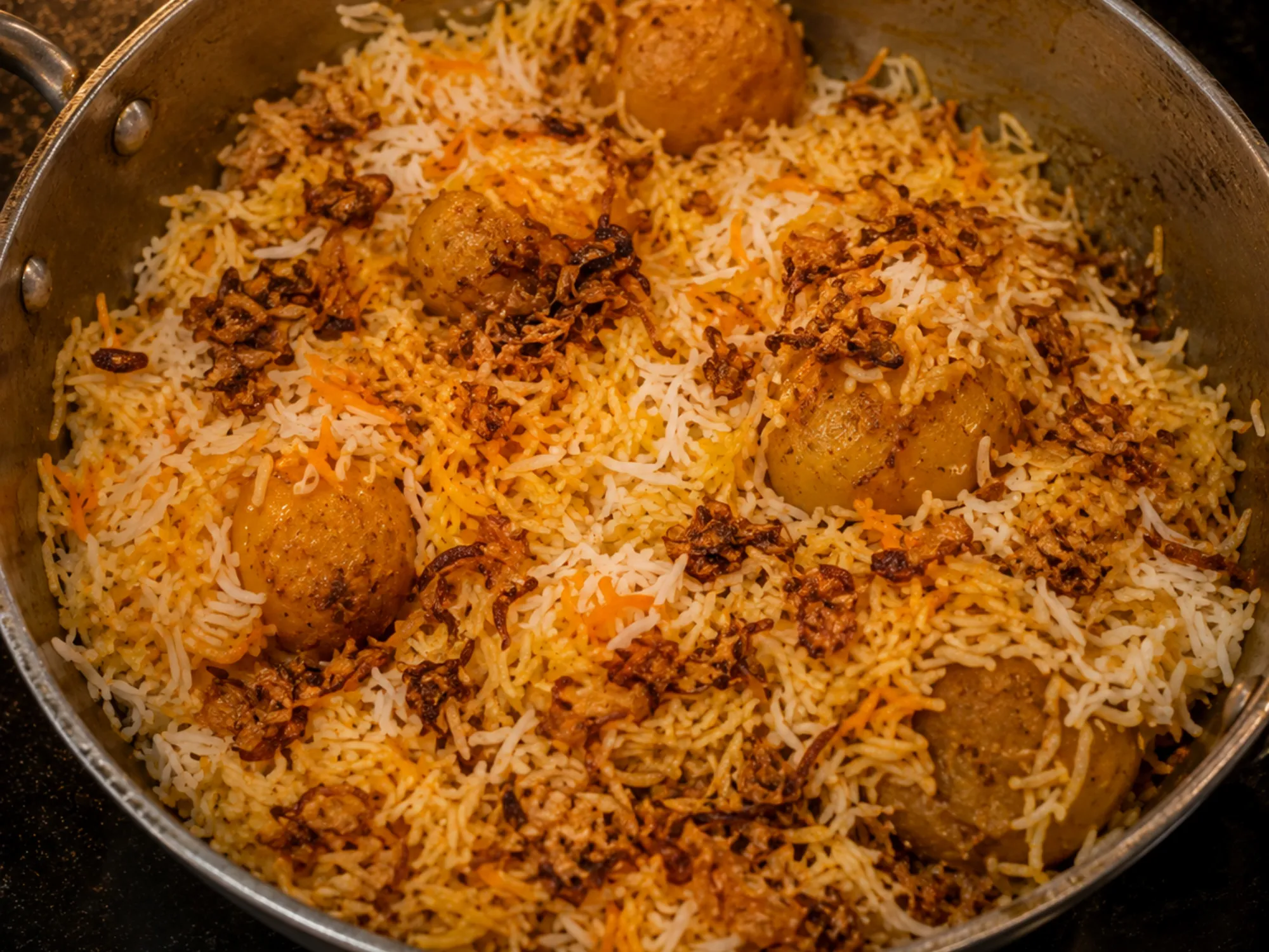 A serving of aloo biryani showing whole browned potato halves under white and saffron-streaked rice, scattered with fried onion
