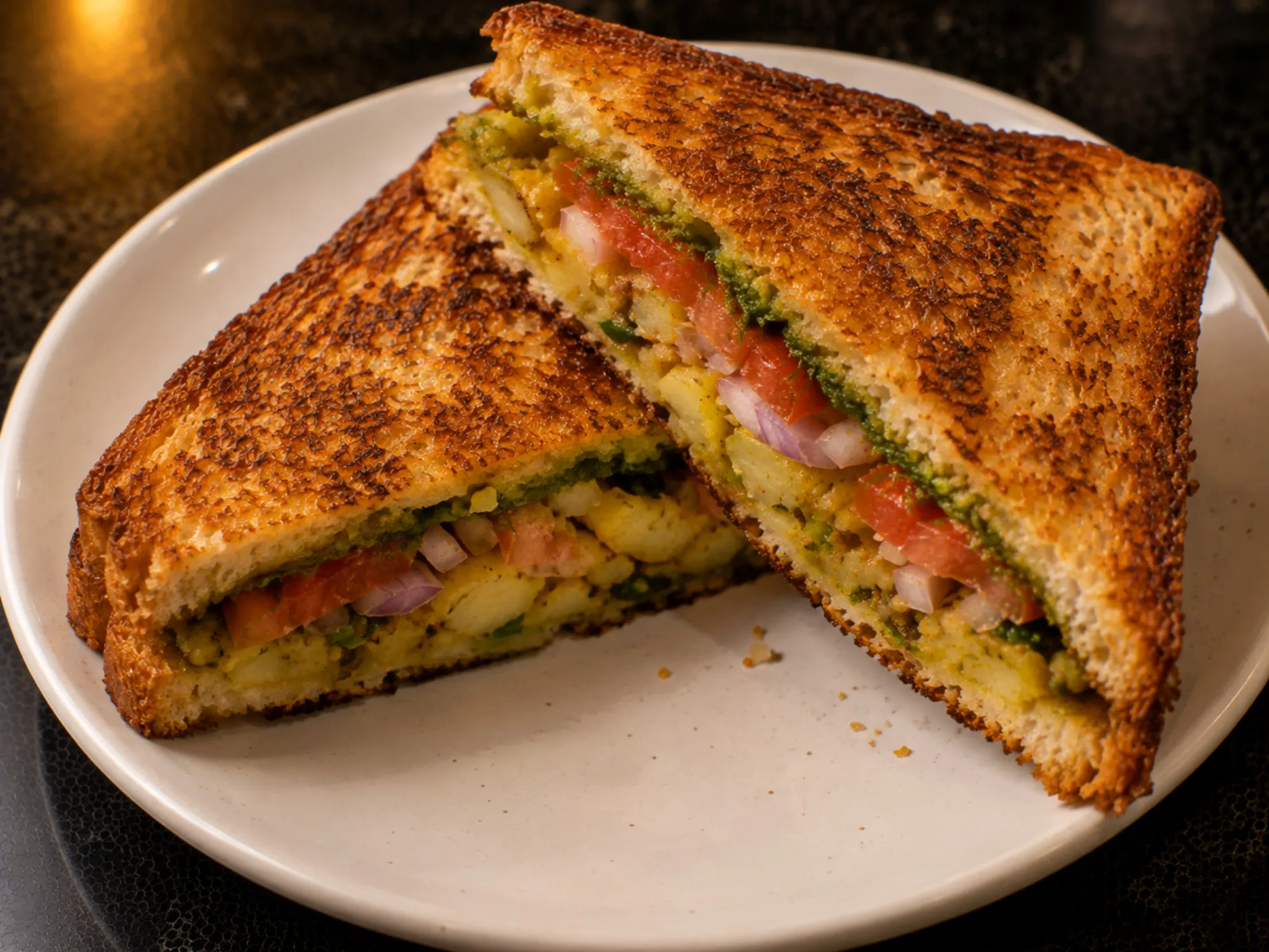 A halved masala toast sandwich showing layers of green chutney, potato, tomato and onion