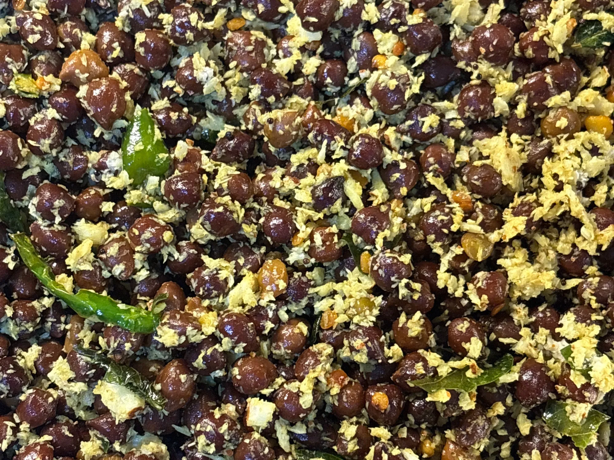 A steel bowl of dark brown chana tossed with grated coconut, curry leaves and coriander