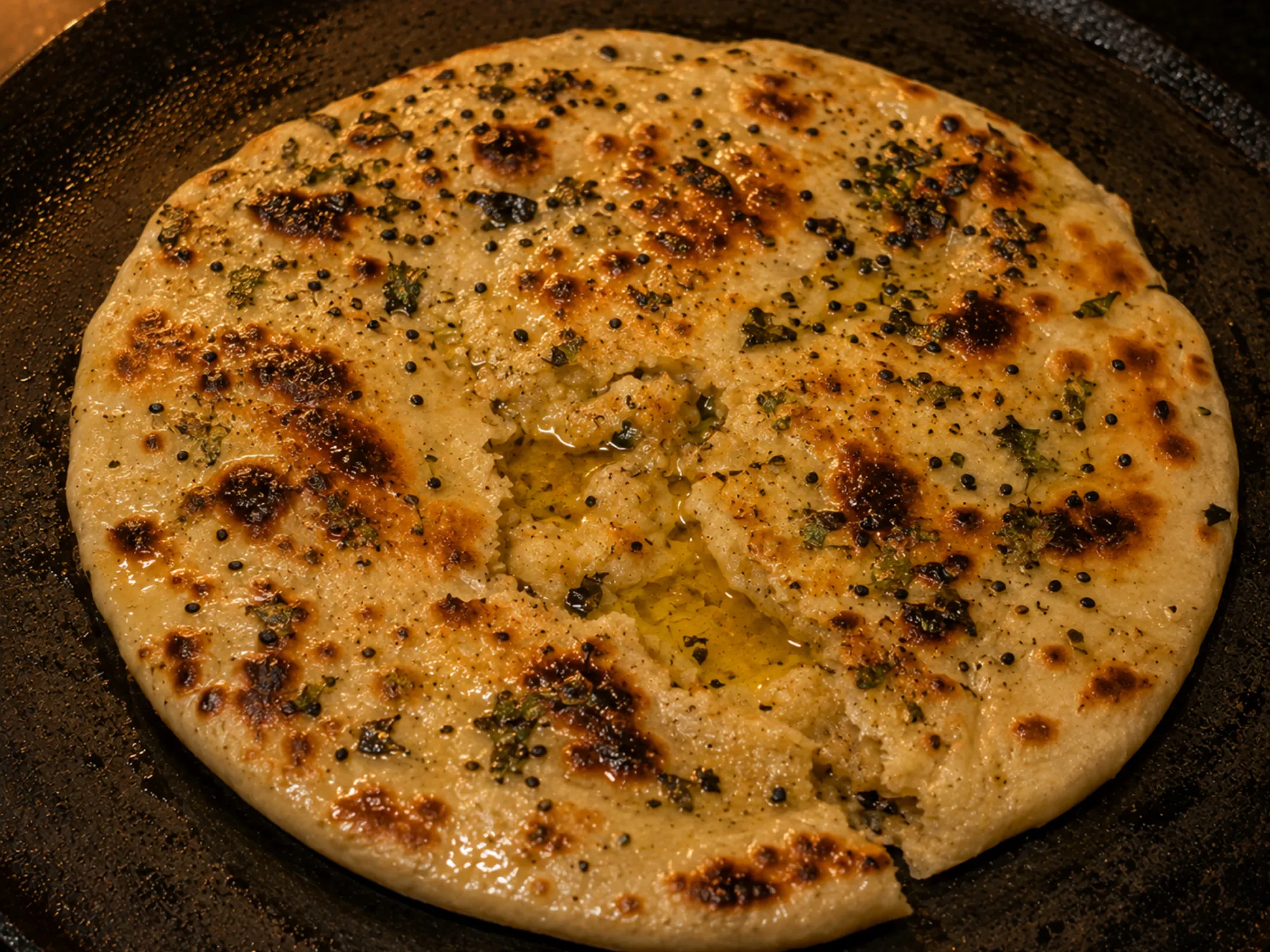 A crisp stuffed kulcha with coriander and nigella seeds on top, crushed open and pooling butter