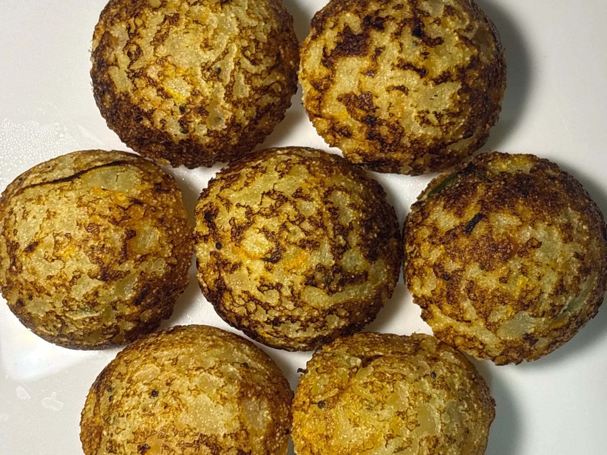 Golden-brown round paniyaram lifted from the dimples of a cast iron appe pan