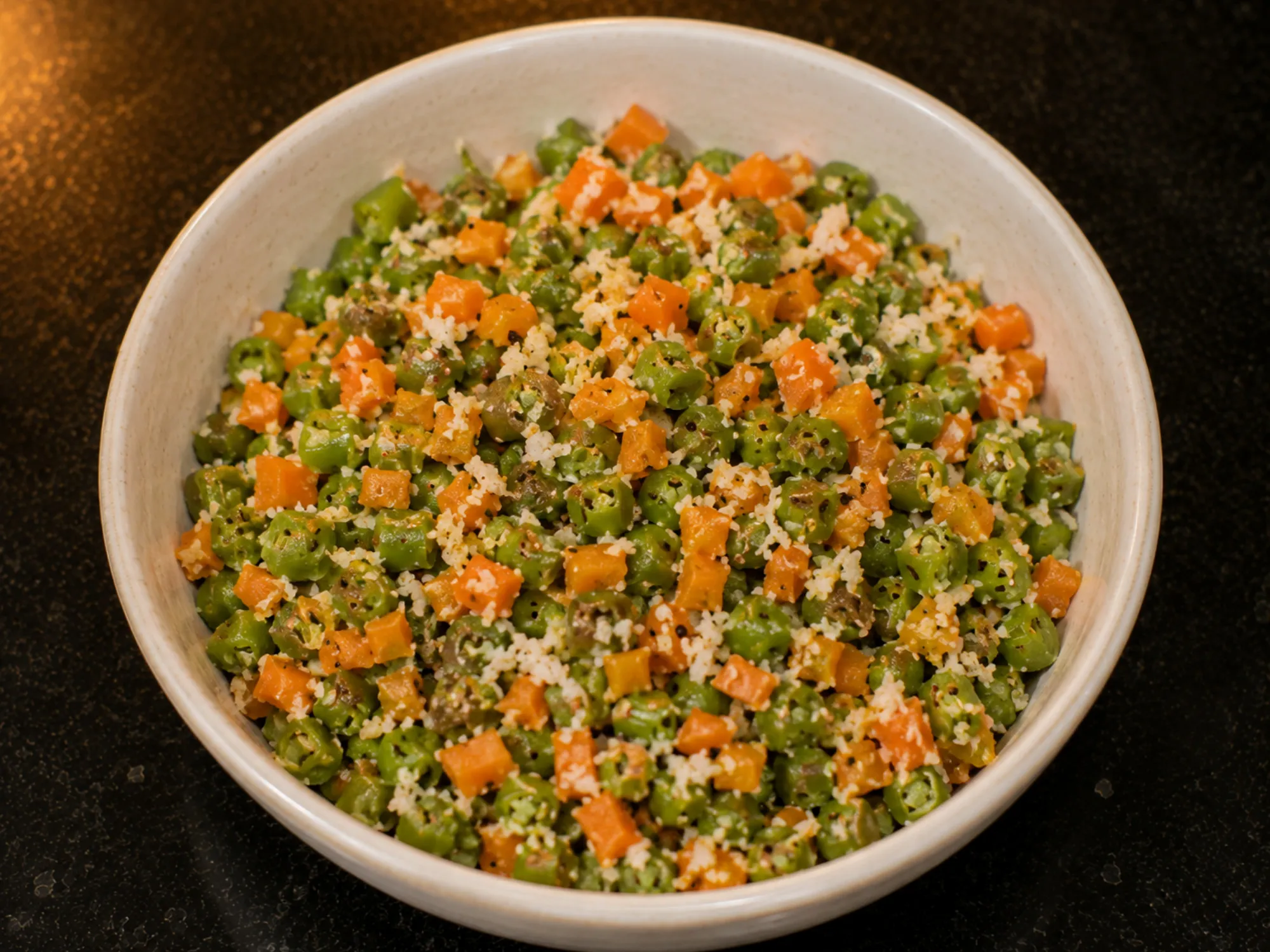A pan of finely chopped green beans and orange carrot flecked with white grated coconut and mustard seeds