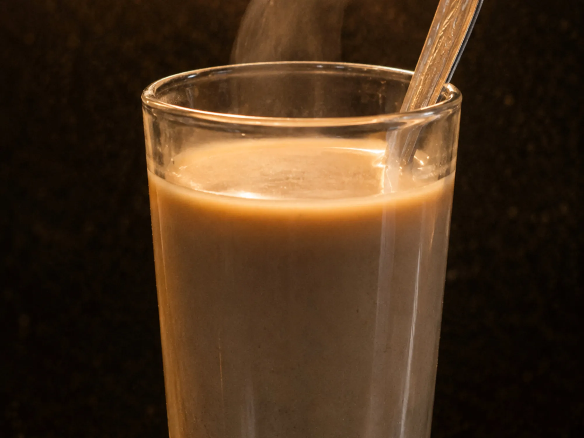 A steel glass of pale brown bajra raab, steam rising, a spoon resting against the rim