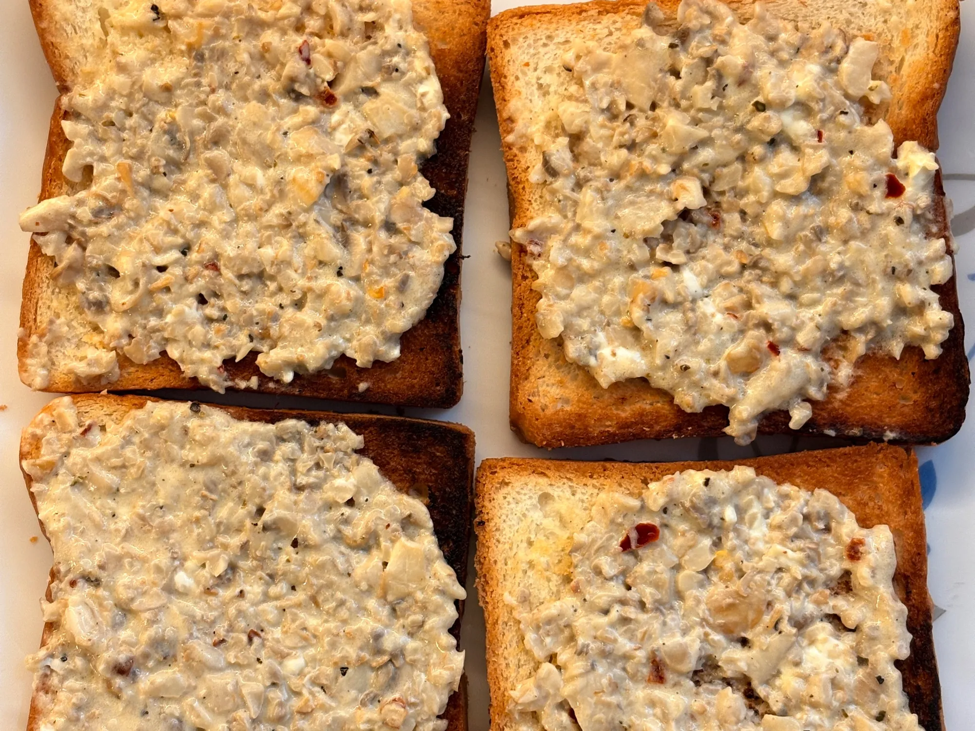 Thick toast heaped with browned sliced mushrooms in a pale creamy sauce, scattered with chilli flakes and spring onion