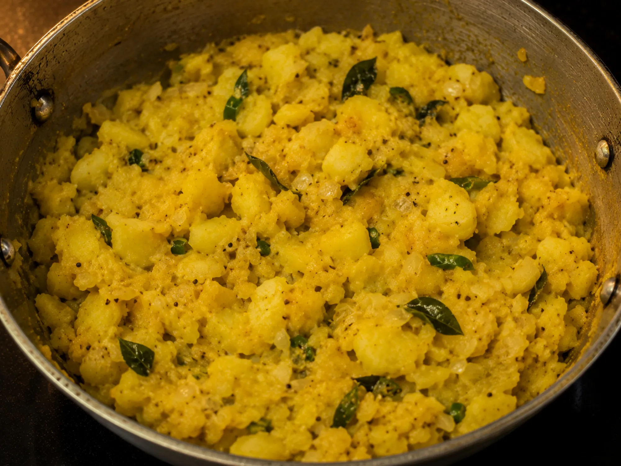 A bowl of soft yellow potato masala flecked with onion, green chilli and curry leaves