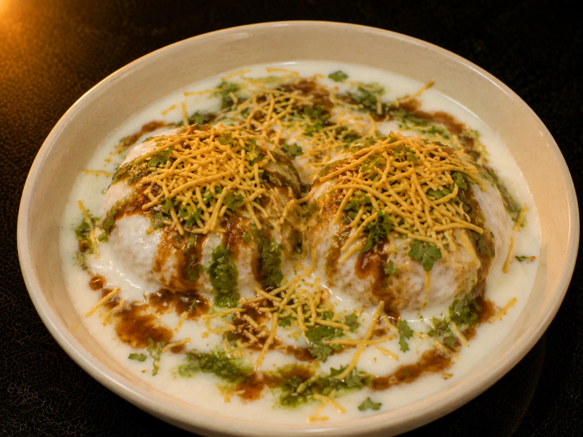 White bread rounds under whisked curd, drizzled with brown and green chutney and topped with sev