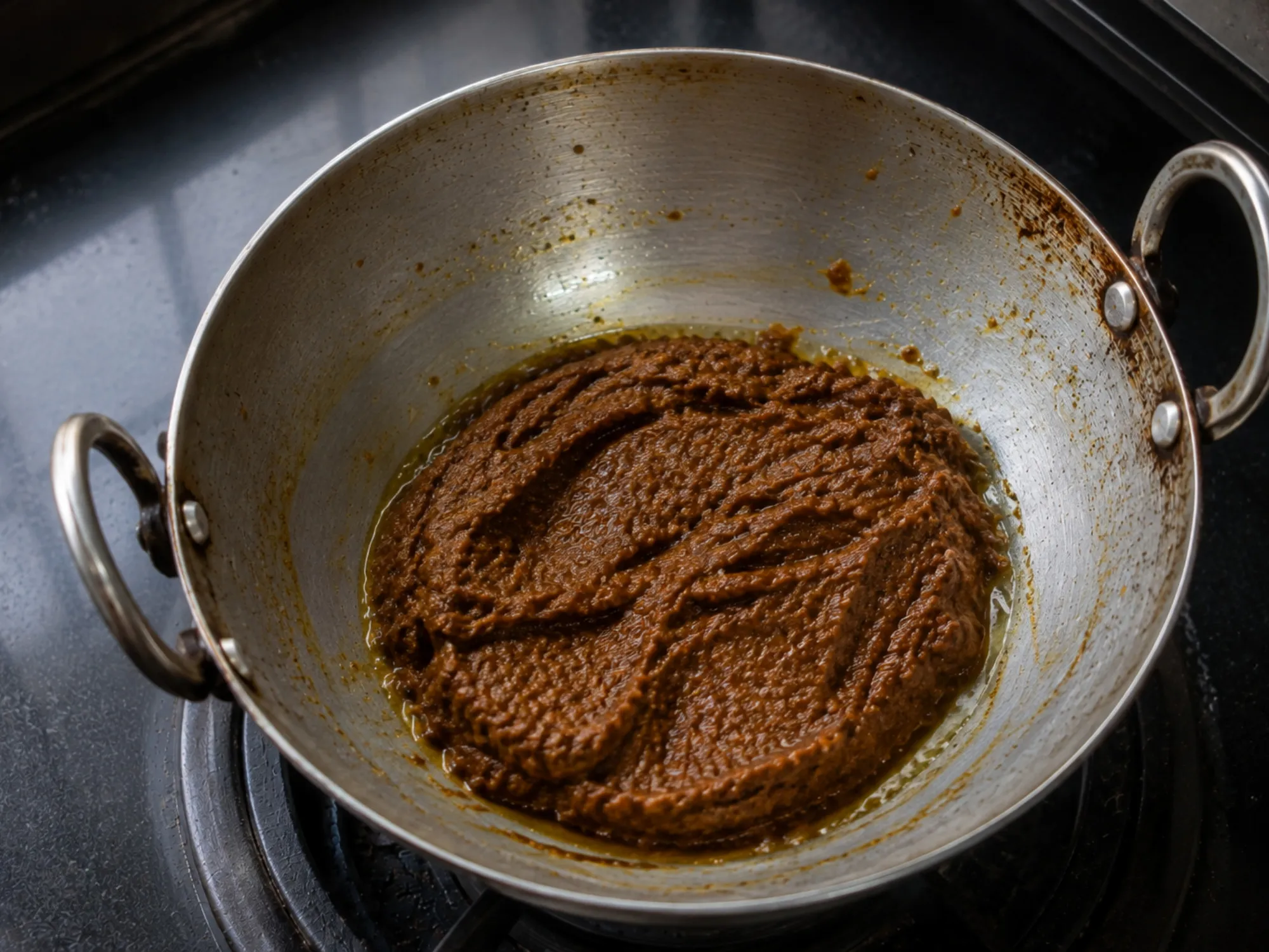 A small steel bowl of dark brown ginger chutney beside a folded pesarattu