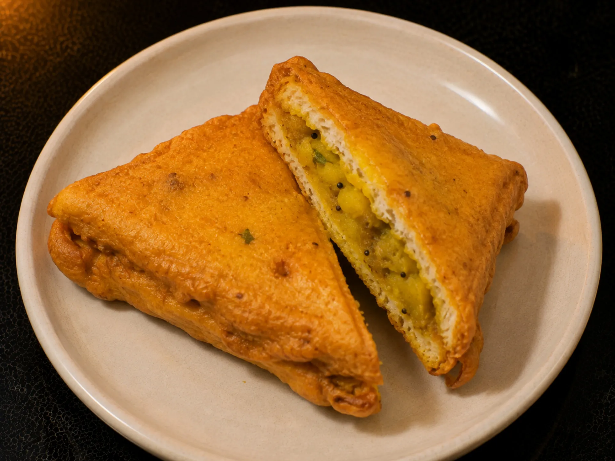 Triangles of golden bread pakora cut open to show the yellow potato filling